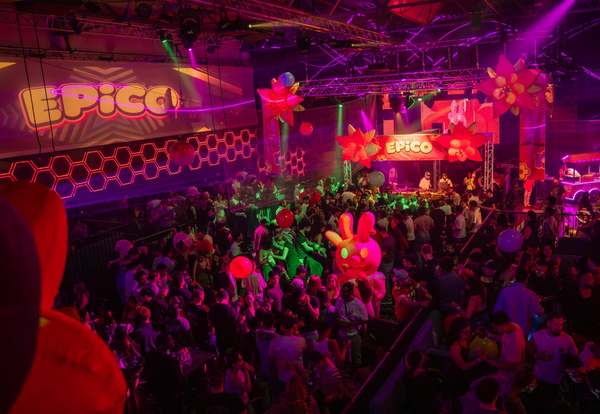 Carnival decor with giant flowers and an EPICO banner above a partying crowd
