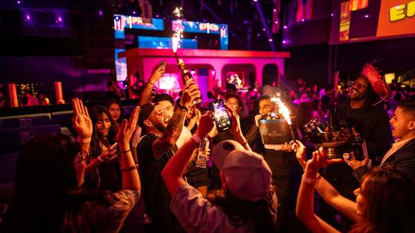 Cheering crowd raising bottles topped with sparklers in front of the pink stage at an EPICO reggaeton party