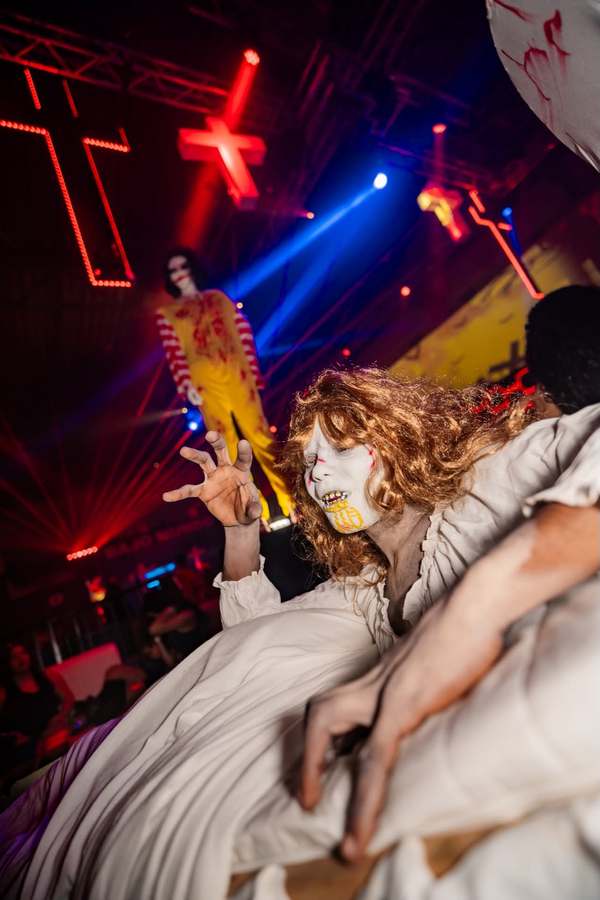 Partygoer in a white dress and skull make-up beneath the red neon crosses of the Halloween party