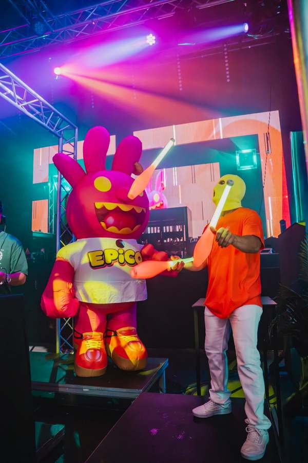 EPICO's giant mascot, an inflatable pink bunny, on stage next to a juggler in a yellow balaclava with glowing clubs