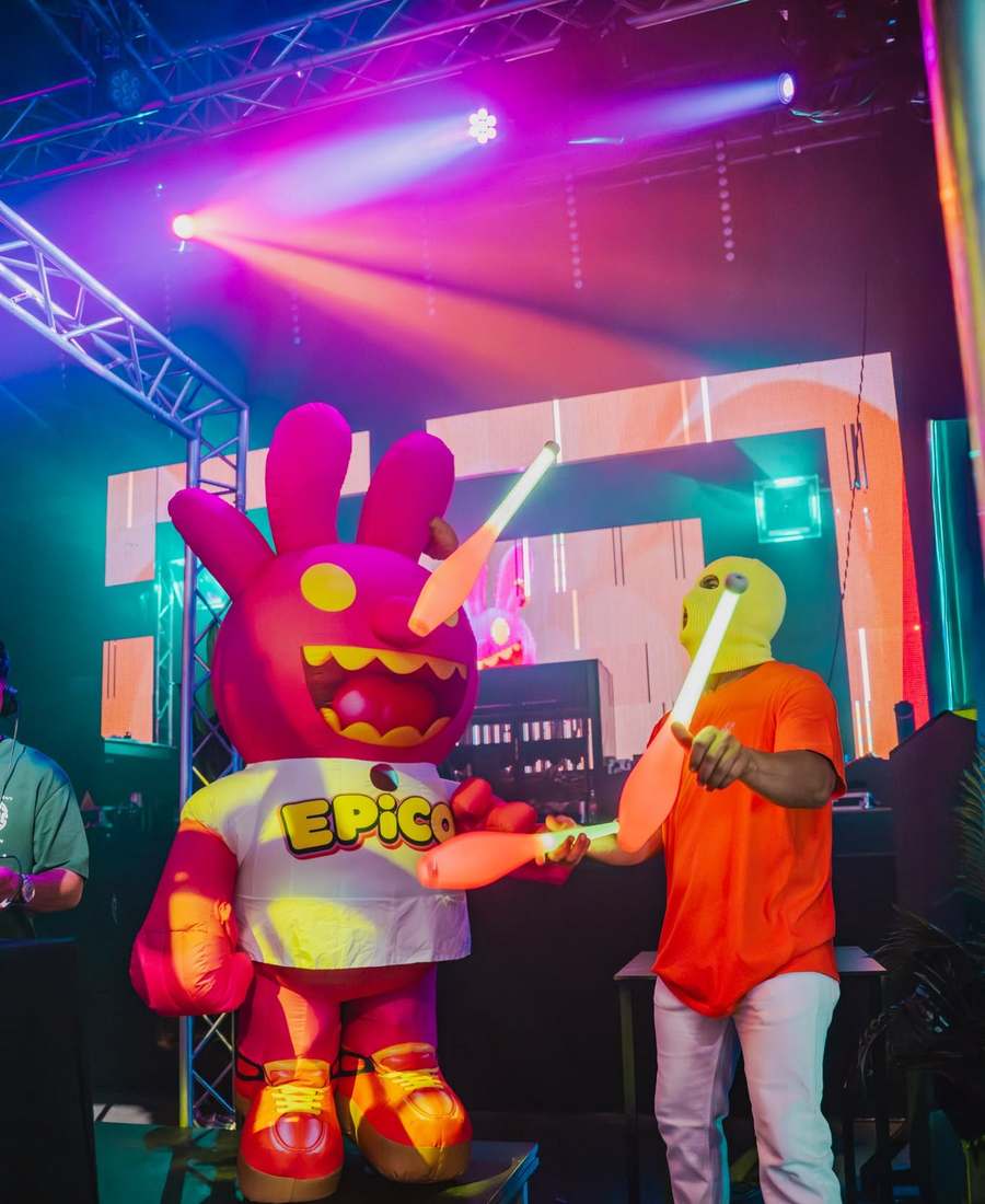 EPICO's giant mascot, an inflatable pink bunny, on stage next to a juggler in a yellow balaclava with glowing clubs
