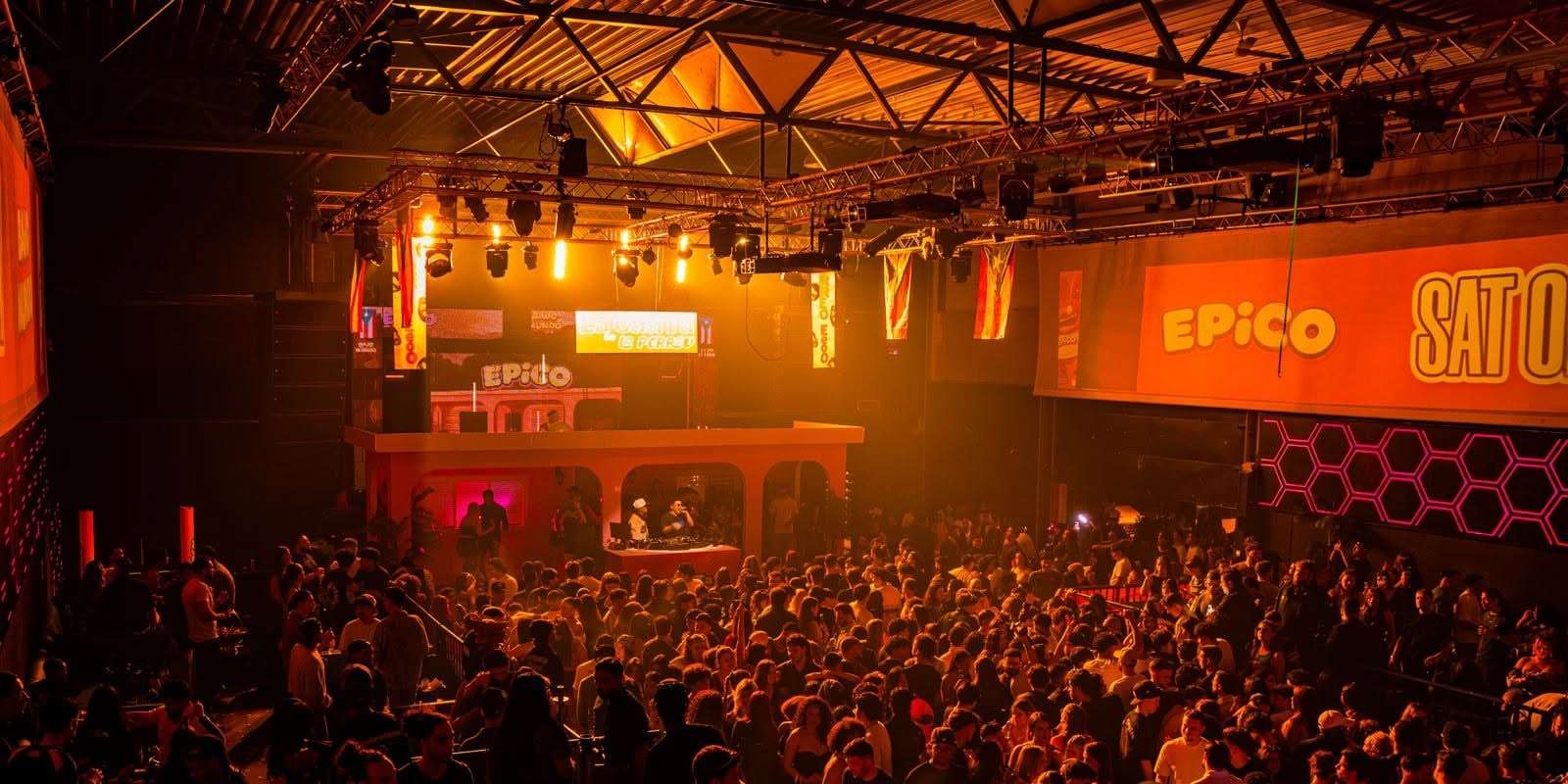Salle comble baignée de lumière orange sous les bannières EPICO, vue depuis le fond de la soirée