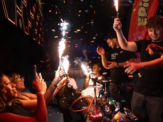 Servicio de botellas con bengalas en una mesa VIP, bajo una lluvia de confeti y una bandera de EPICO